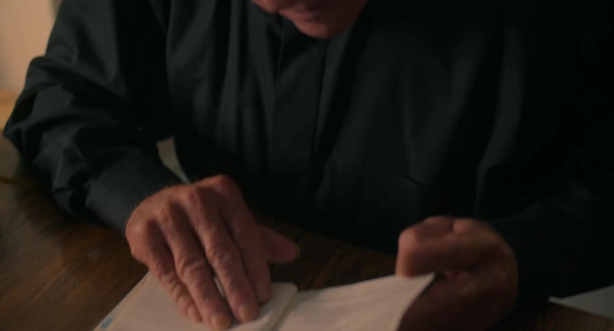 An elderly man reading from a book while sitting down