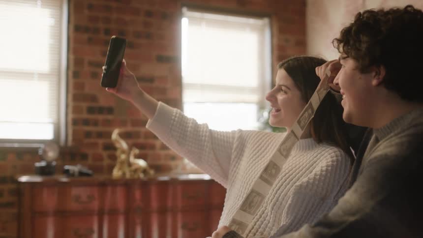 A young man and woman posing for a selfie while the man holds up a roll of photos