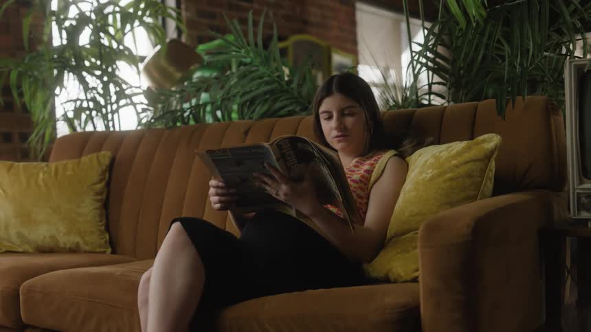 Joyful woman sitting on the couch reading a magazine in the living room