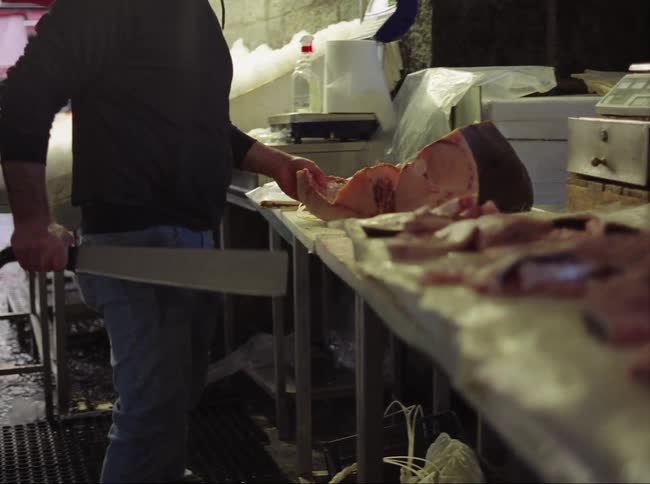 A butcher uses a large knife to cut meat indoors during the day