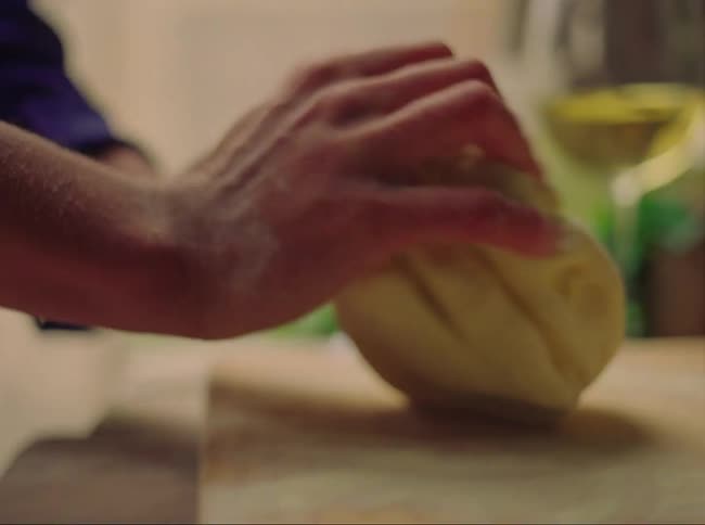 A person kneads dough on a wooden cutting board