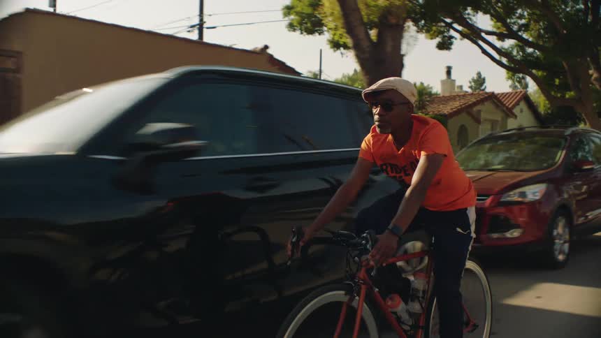 A man rides a bicycle along a road through a residential neighborhood during the day