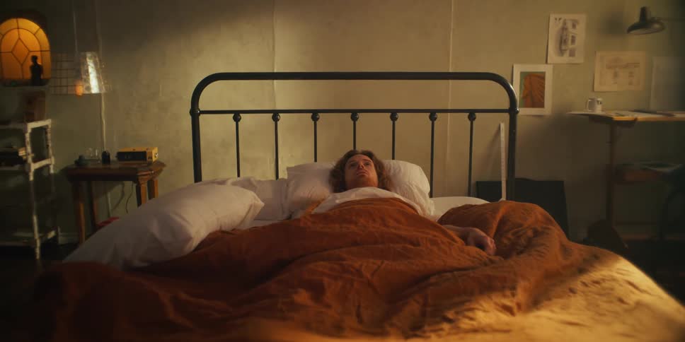 Man lies in bed as the bed slides across room toward wall