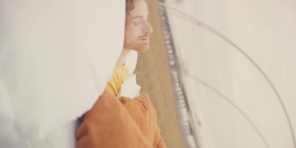 A man sleeping in a bed in a field with yellow grass starting with an upside down angle then reverting to normal