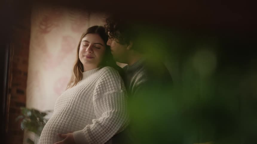 A straight couple with the woman pregnant kiss and she rubs her pregnant tummy