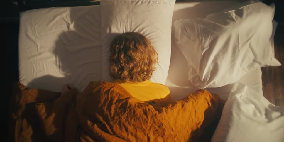A woman sleeping face down on a bed turning as she starts to wake up