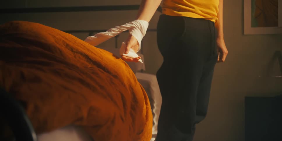 A man stands up from bed despite his arm being tied in a bedsheet