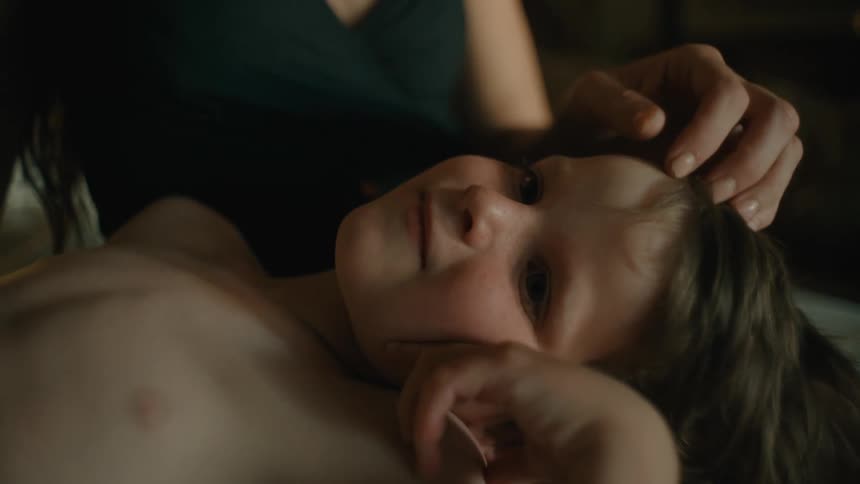 Child laying on mothers lap as she strokes the childs hair in a dimly lit room