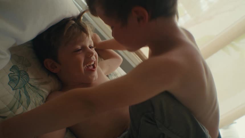 Two boys are play fighting on a bed inside
