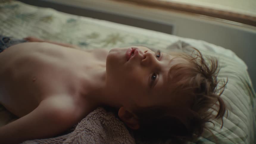 A young boy lying in bed staring at the ceiling