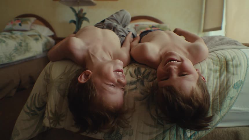 Two boys without shirt on laying on the bed laughing