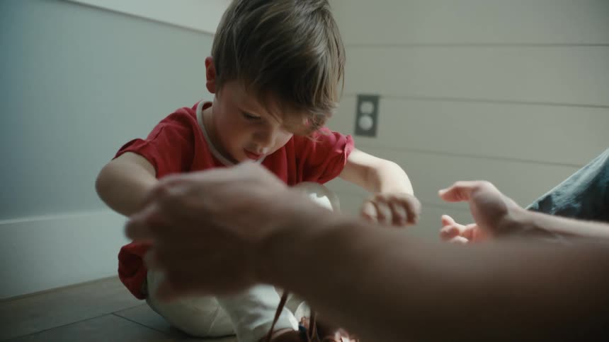 Father assisting his son in tying his shoes both seated on the floor