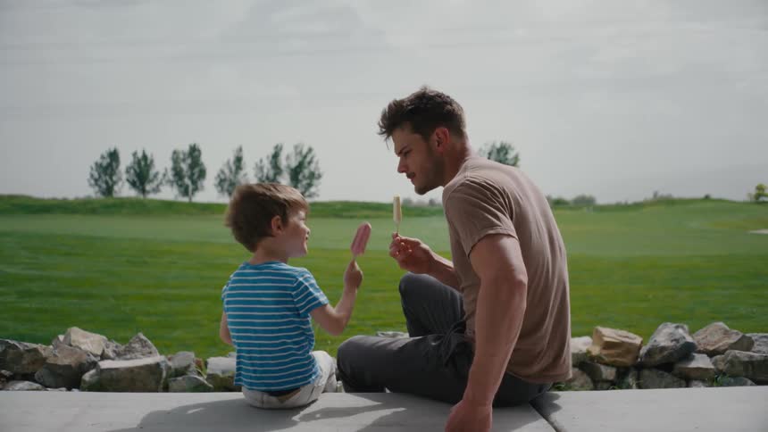 Father and son hanging out and eating popsicles outdoors