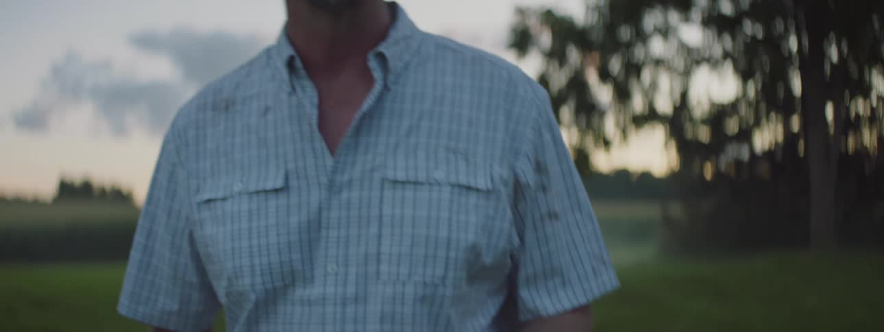 A man is walking through a country field holding a small piece of paper and reading it as he is in deep thought