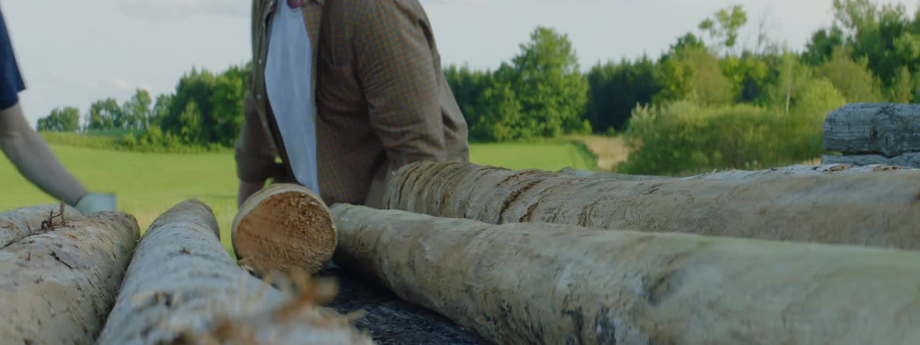 Two men move logs from wooden platform near field