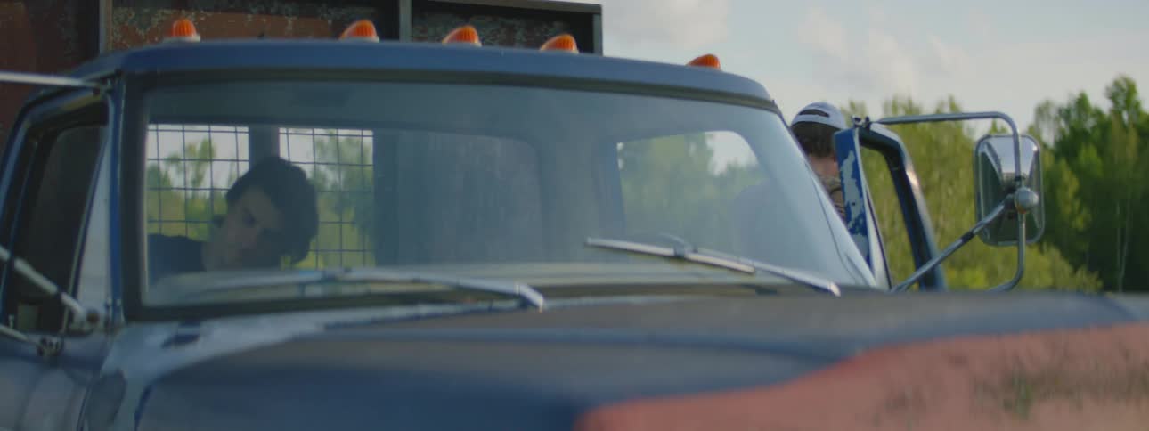 Two men park a truck in a field and carry lumber