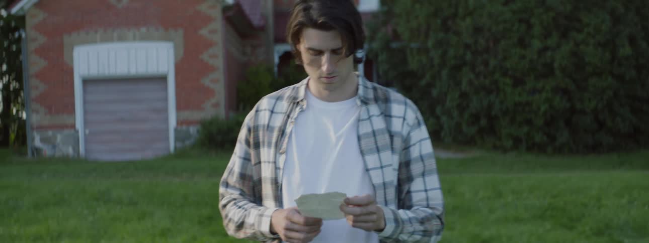 Worried man holding and reading a piece of paper walking in front of a house