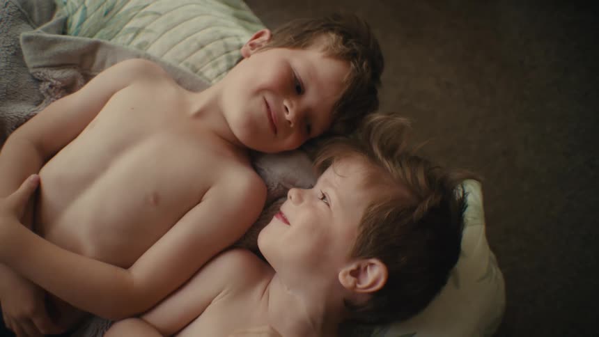 Two siblings make faces and play together while lying on bed