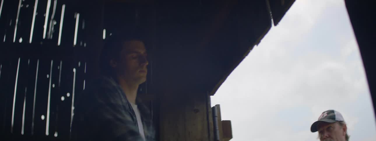 A man handing hay bales to his son in a barn for loading