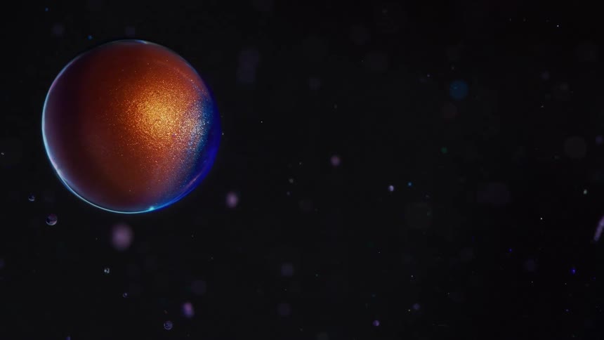 A colorful and sparkly sphere rolling across a black screen with small particles in the background