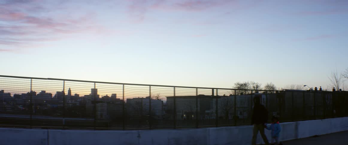 A man and child walk past a fence at dawn