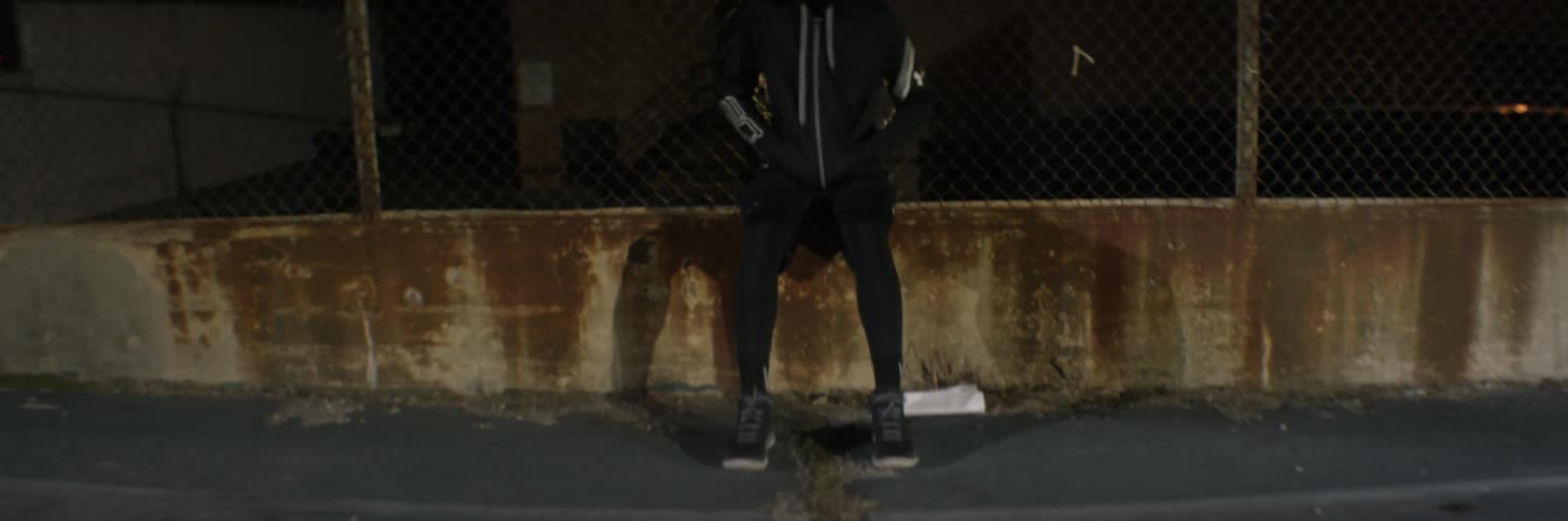 A man wearing a hooded jacket sits in front of a crack in asphalt