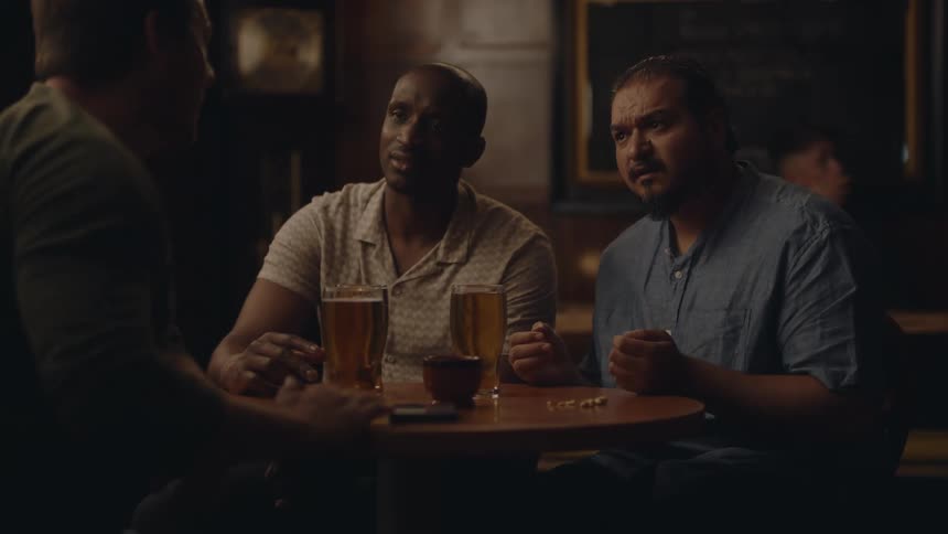 Three friends sitting at a restaurant table with alcoholic drinks in their glasses as they converse before one of them gets up and walks away