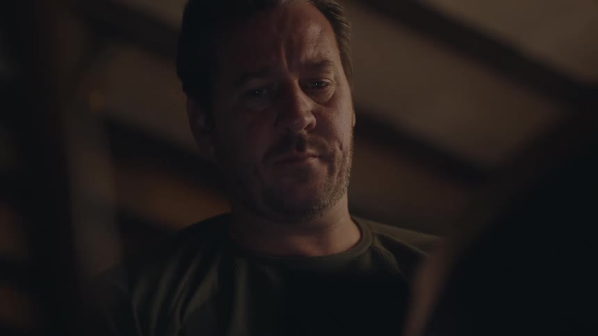 Man sitting indoors with his face down looking at something before looking up and speaking to someone