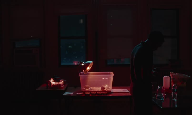 Boy standing in a classroom at night preparing a water bottle next to a lit up plsatic bin with a chick in it