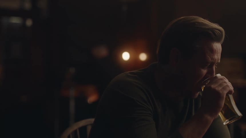 Man sits at table in dark room drinking alcohol