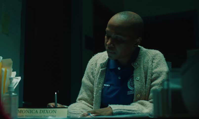 A woman sitting at her desk writing with a pen as she is looking down then picking up her head and looking forward concerned