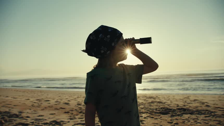 Kid plays with spyglass while standing on the beach on a sunny day
