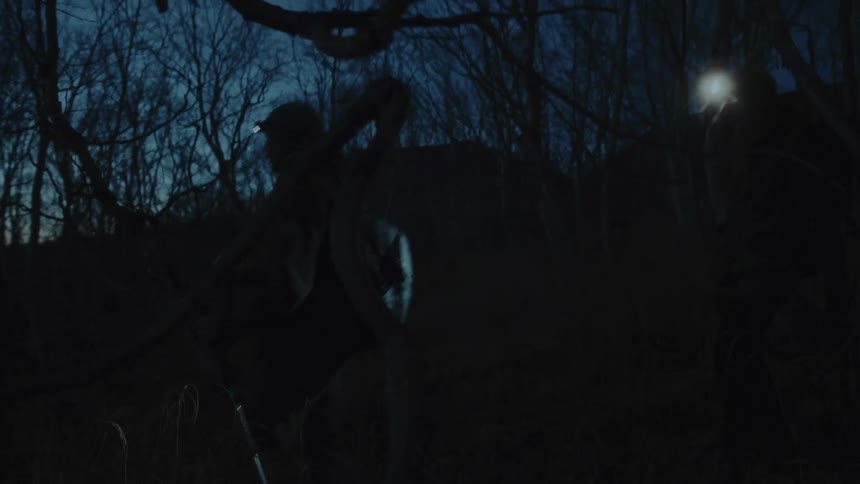 A man wearing a headlamp walks through a dark forest at night