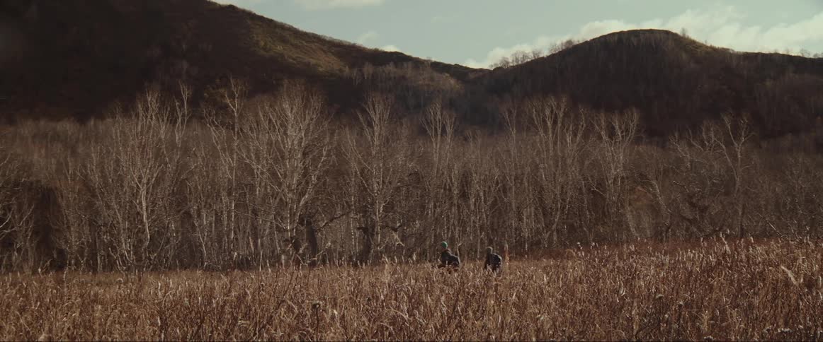 A pair of hikers hike through a large field in the wilderness during the day
