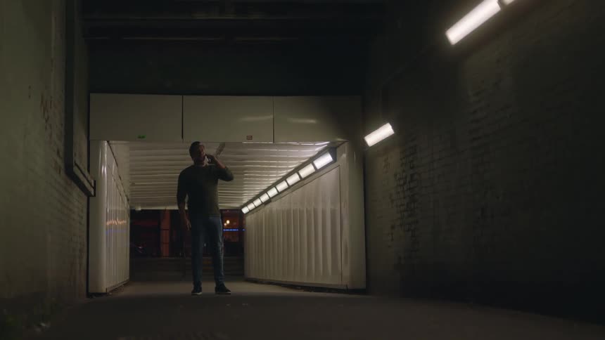 A man standing in the middle of a tunnel and speaking on his phone at night
