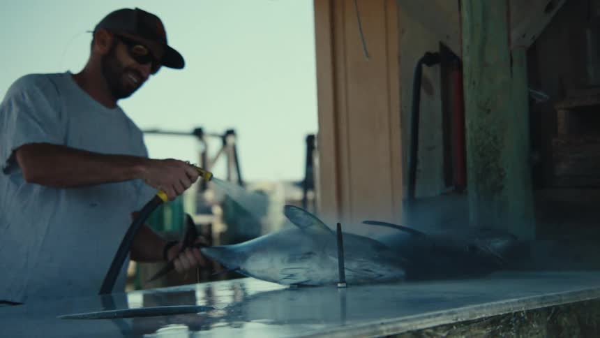 Man smiles while standing outdoors and spraying large fish with a water hose