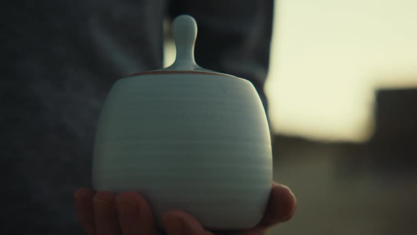 White man holding a white clay pot on his hand outdoors