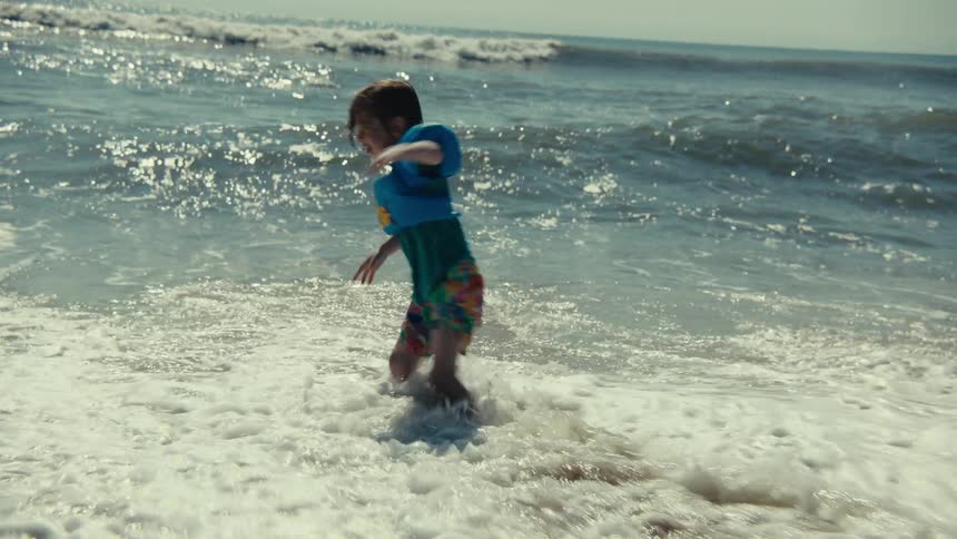 A child plays in the ocean tide while wearing a floatation device