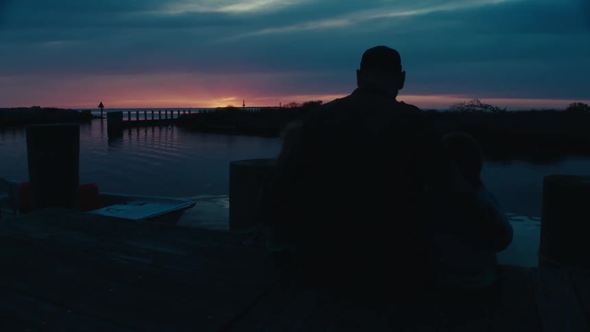 A man is standing near a lake during sunset