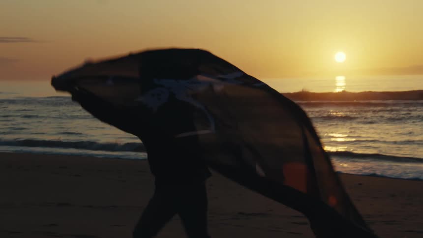 A silhouette of a young child running with a sheet behind them on the beach as the sun sets