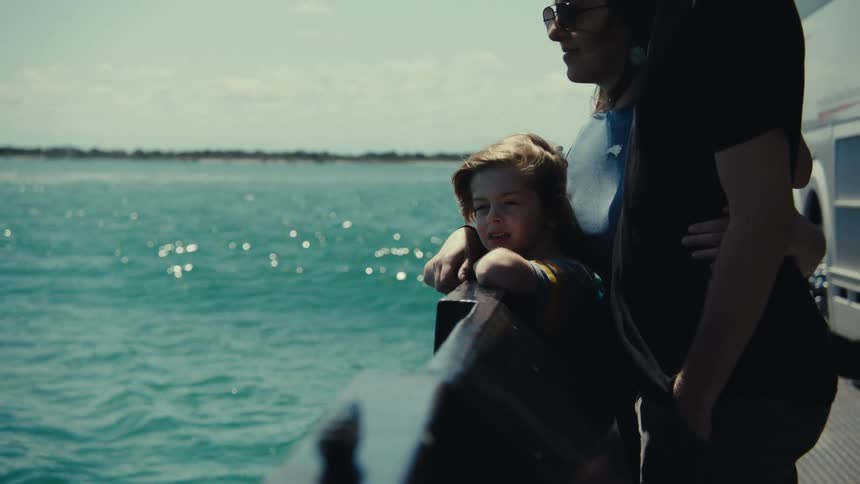 A man a woman and a young girl travel across the sea on a boat looking at the sea from a security rail