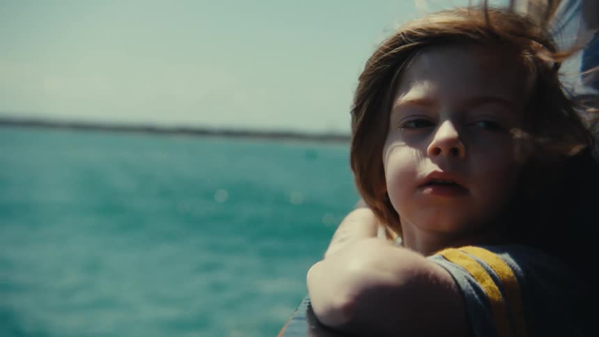 A close up of a young boy standing in front of his mother on a boat on the ocena