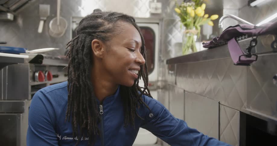 Woman chef kneeling and opening a cabinet while smiling and laughing