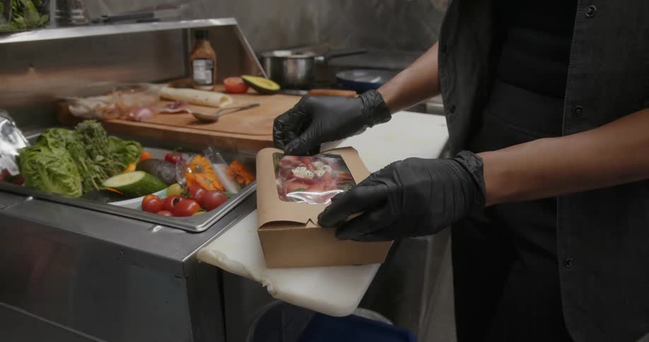 A close up of a person preparing a salad in a food box securing both ends