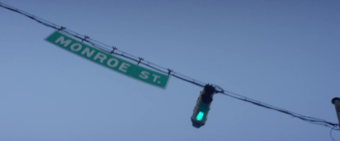 A street sign is next to the traffic lights on a clear day
