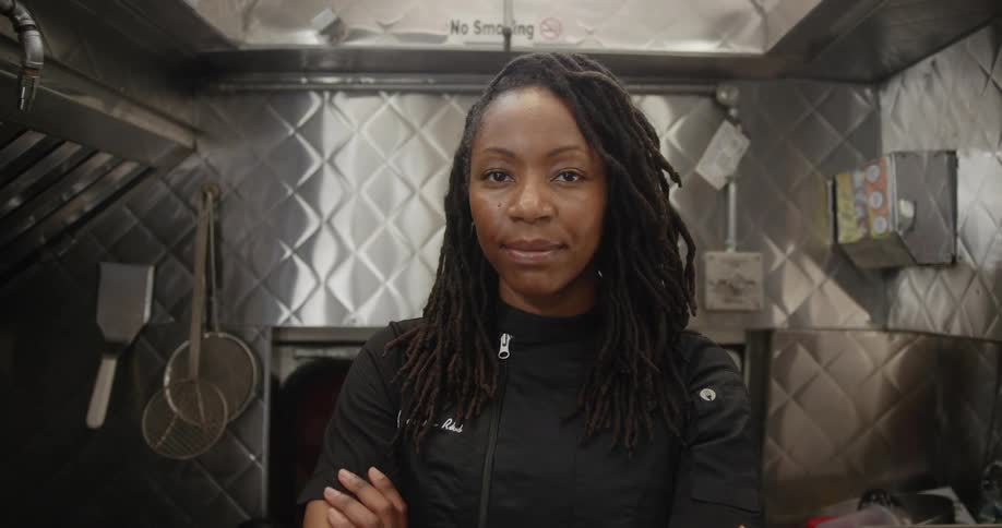A woman in a silver kitchen crosses her arms smiles and poses in a power stance
