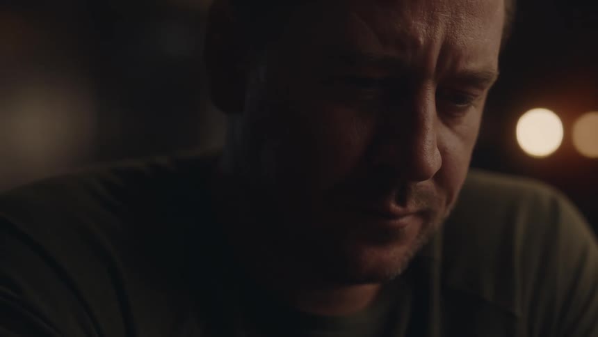 A man sitting in a bar at night sighs and takes a sip from a beer glass