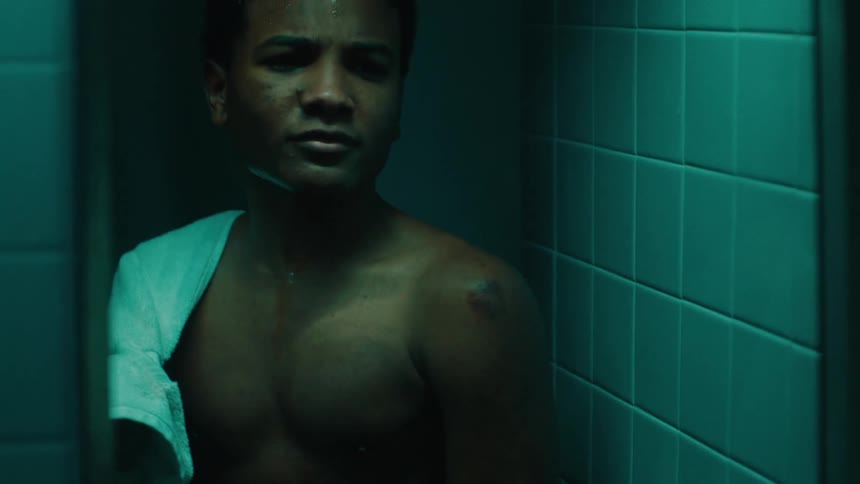 A boy looks at a bruise on his shoulder in a mirror sweating and looking in pain