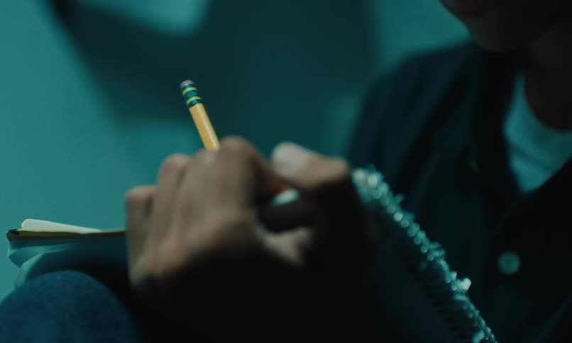 A close up of a person writing with a pencil on a notebook