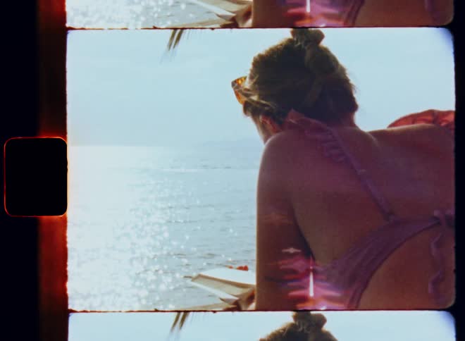 A close up of a woman laying down on her stomach reading a book looking out over the ocean